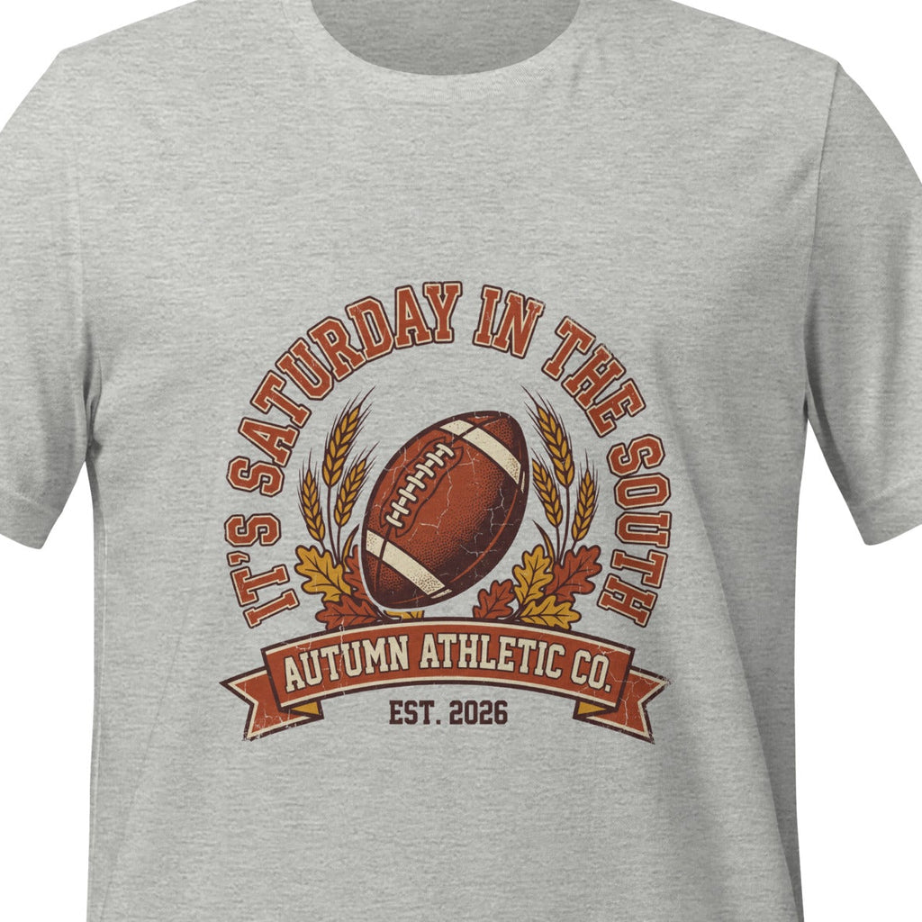 Athletic heather unisex t-shirt printed with a vintage arched badge reading It's Saturday in the South, curving over a football with wheat stalks and autumn leaves
