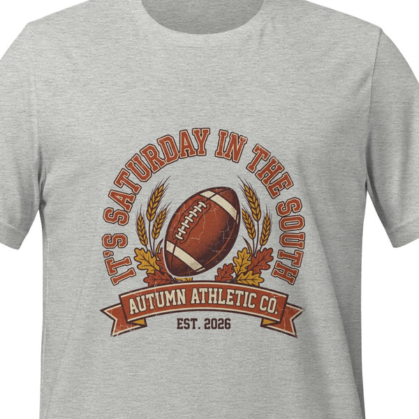 Athletic heather unisex t-shirt printed with a vintage arched badge reading It's Saturday in the South, curving over a football with wheat stalks and autumn leaves